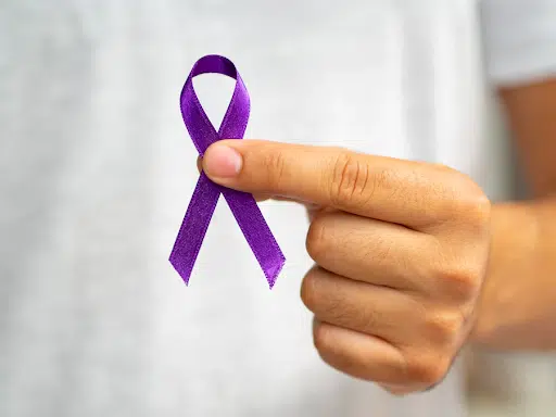 Imagem de uma mão masculina segurando uma fita roxa para simbolizar o Dia da Campanha Educativa de Combate ao Câncer