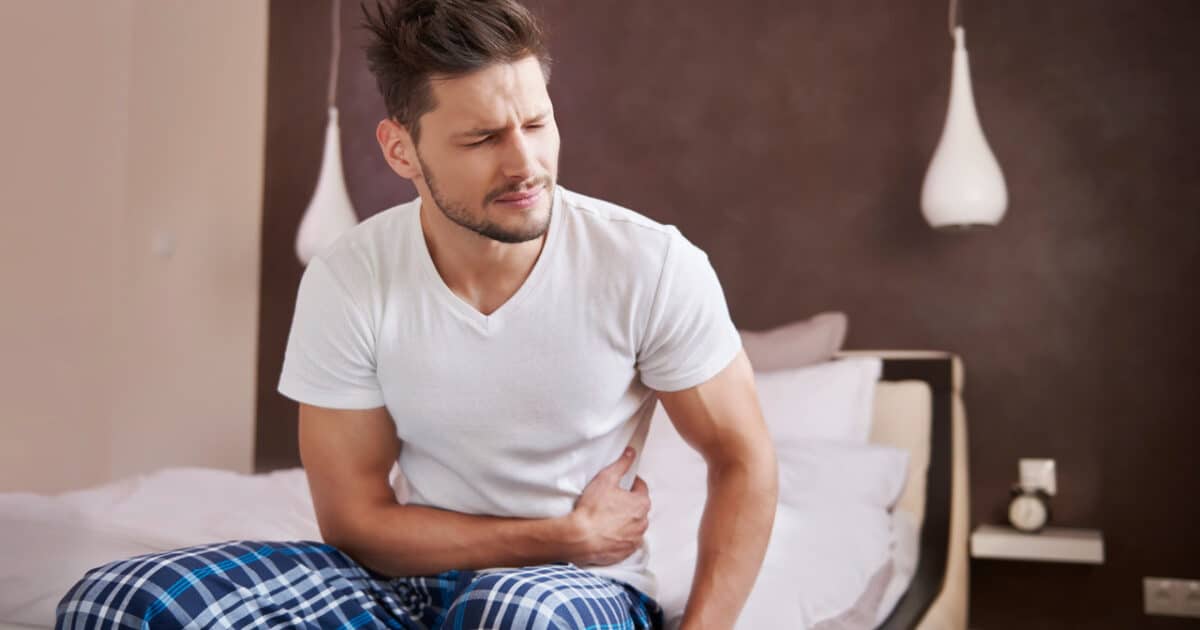 Imagem de um homem sentado na cama com dor na bexiga para simbolizar o tumor na bexiga