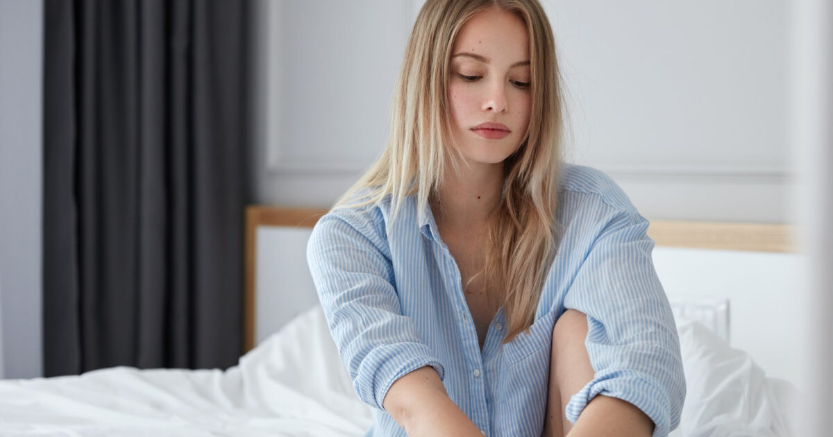 Imagem de uma mulher sentada na cama com uma expressão triste para simbolizar o desejo sexual hipoativo