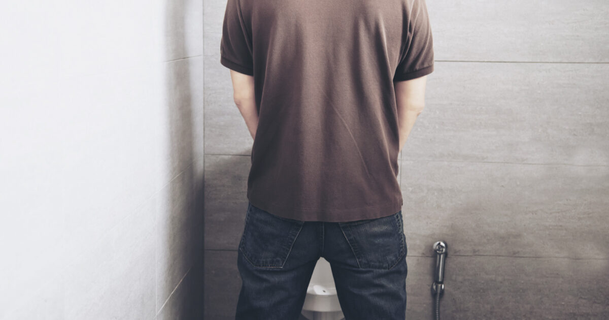 Imagem de um homem de costas, no banheiro, fazendo xixi ára simbolizar a urina roxa
